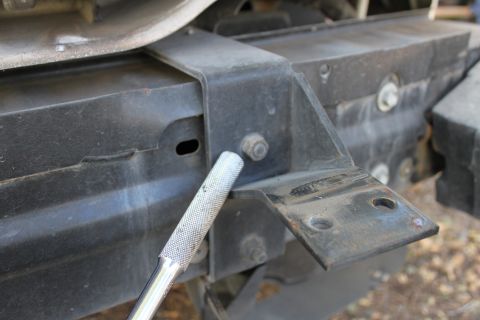 2003 Ford Crown Victoria - A socket wrench tightens a bolt on a black metal push bar mounting bracket attached to a vehicle's frame.