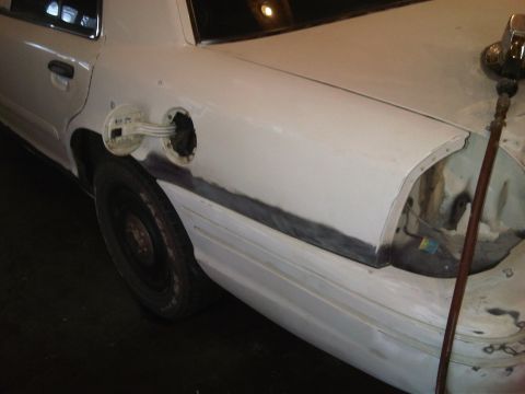 2003 Ford Crown Victoria - Bodywork in progress on a white sedan, showing primer and sanding marks on the rear fender.
