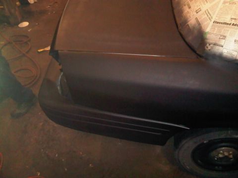 2003 Ford Crown Victoria - Rear quarter panel of a dark sedan, possibly undergoing repair or painting, with a primer finish.