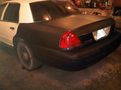 2003 Ford Crown Victoria - The rear of a two-tone Ford Crown Victoria shows a flat tire and a license plate.