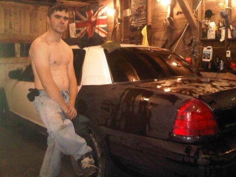 2003 Ford Crown Victoria - A man poses next to a dark sedan with a white roof inside a cluttered garage.