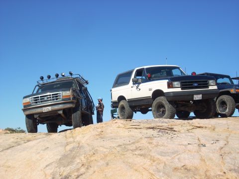 1989 Ford Bronco - Two Ford Broncos and a Jeep are parked on a rocky incline under a clear blue sky.