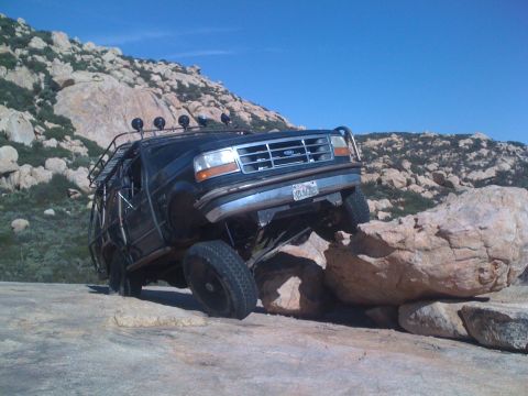 1989 Ford Bronco - This modified Ford Bronco is navigating a rocky trail with its tires on large boulders.