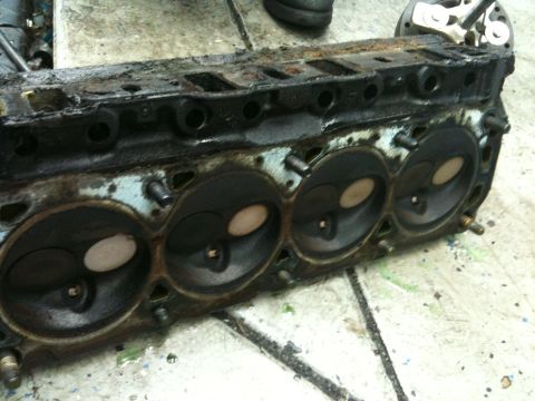 1990 Ford Bronco - A heavily used engine cylinder head sits on a workbench, showing signs of wear and tear.