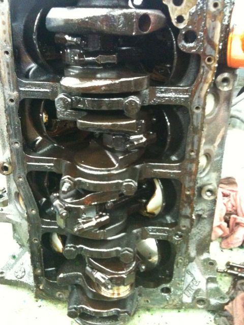 1990 Ford Bronco - Close-up view of an engine block's internal components, including the crankshaft and connecting rods, all coated in oil.