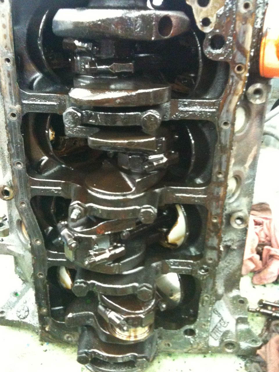 Engine block with crankshaft and connecting rods, covered in oil. Visible text: SUPERMOTORS.NET