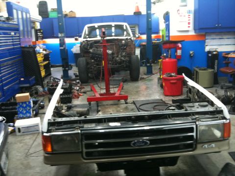 1990 Ford Bronco - Front view of a 1990 Ford Bronco in a garage, engine removed for repair.