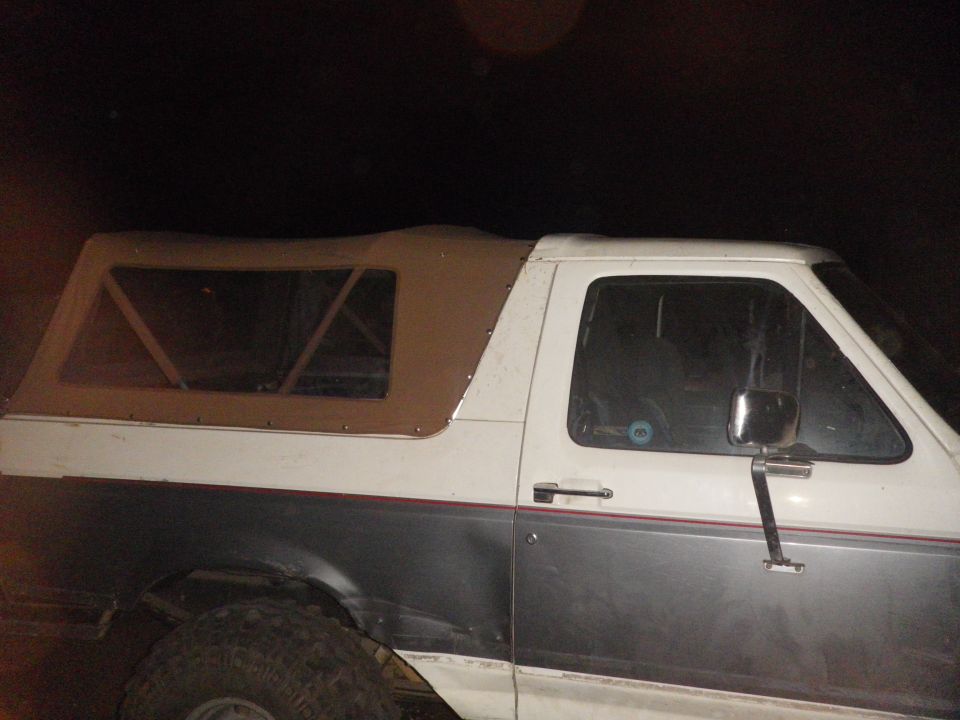 Two-tone Ford Bronco with tan soft top over rear tub, driver side at night