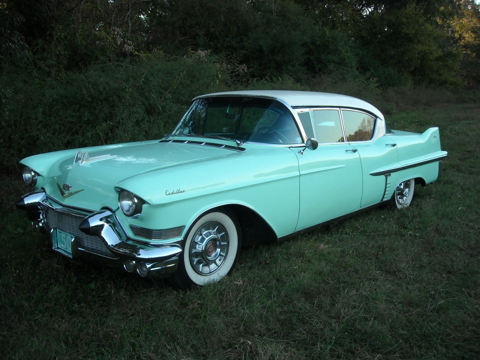 1957 Cadillac Coupe de Ville, turquoise and white, parked on grass with trees in background