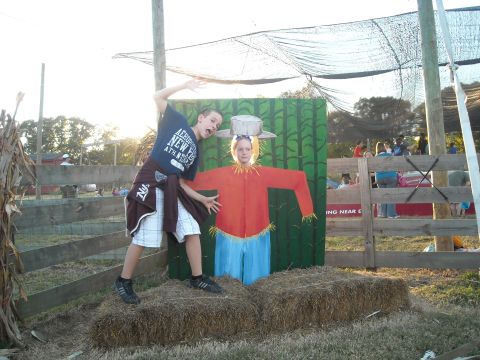 1979 Ford F-150 - A boy poses playfully next to a scarecrow cutout at an outdoor event, with hay bales and a wooden fence visible.