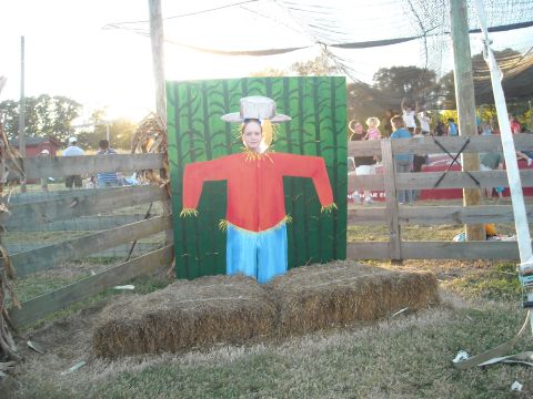 1979 Ford F-150 - A person poses in a scarecrow cutout at a fall festival, with hay bales in the foreground and a wooden fence in the background.