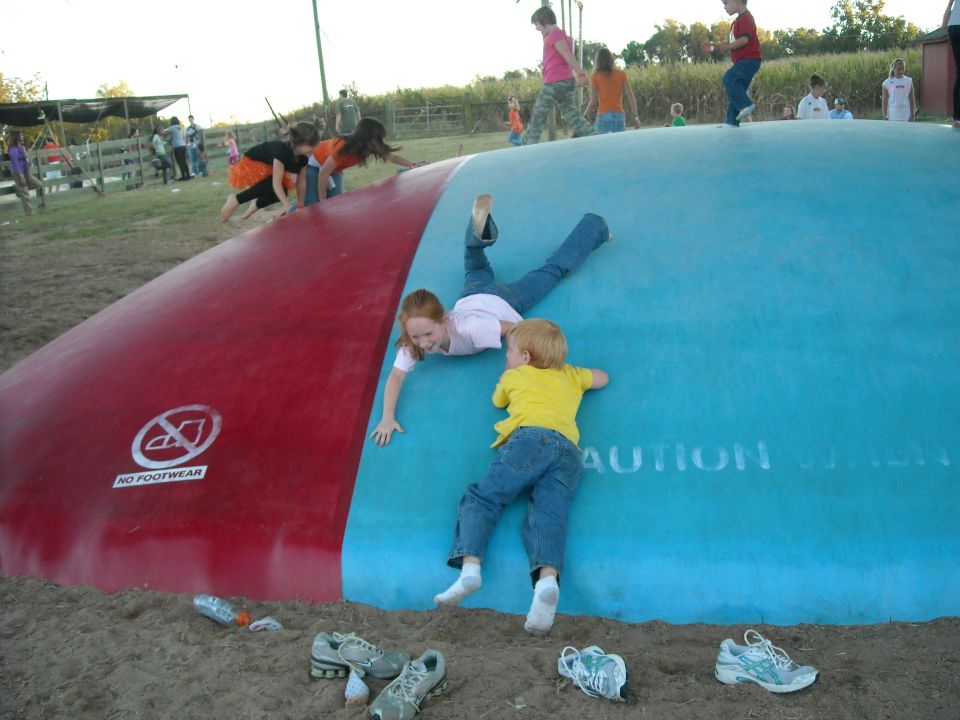 Children climbing on a large red and blue inflatable cushion with 'NO FOOTWEAR' and 'CAUTION' text visible