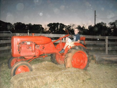 1979 Ford F-150 - A young boy sits on a vintage red tractor, resting on hay bales as dusk settles.