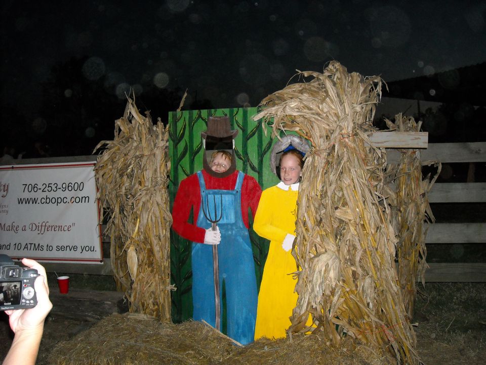 Cardboard cutouts of a farmer and a girl in a yellow dress stand behind hay bales and corn stalks