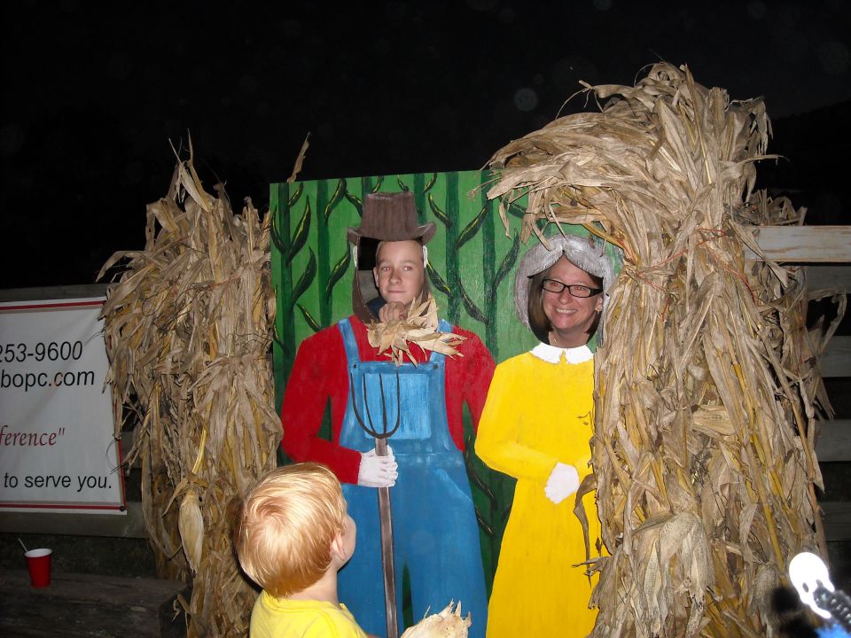 Kid looks at cardboard cutout of farmer and woman in yellow dress, surrounded by corn stalks