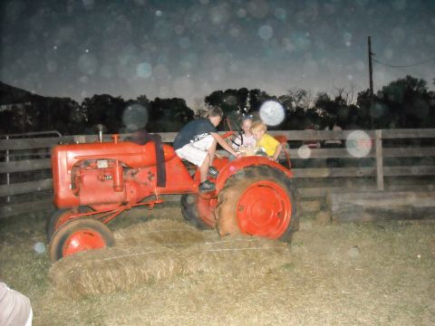 1979 Ford F-150 - Three children ride on an orange tractor in a grassy area with a wooden fence in the background.