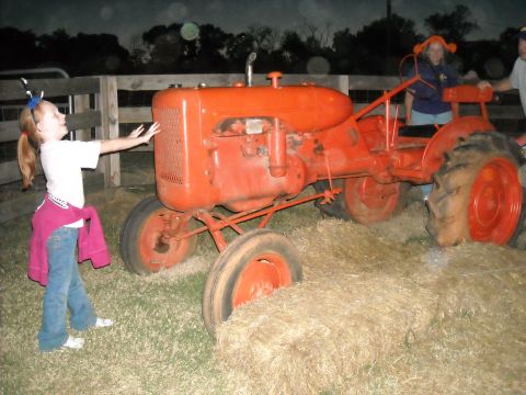 1979 Ford F-150 - A girl interacts with an orange tractor while two adults stand nearby in a field with hay bales.
