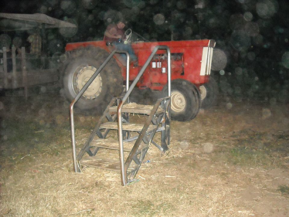 Man sits in a red tractor with large rear tires. A metal staircase is in front