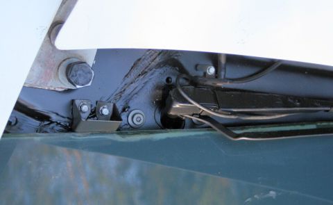1976 Ford Ranchero - Close-up of the freshly black-painted cowl and windshield lower edge with the hood raised, showing brushed seam sealer, a bolted black hood…