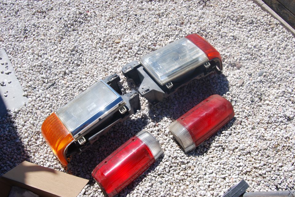 Two headlight assemblies and two taillight assemblies are laid out on a gravel surface