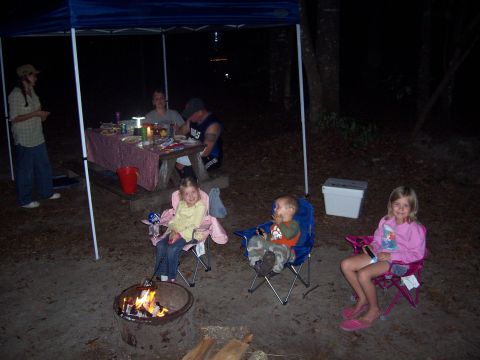 1994 Ford Bronco - A family enjoys a nighttime camping trip around a fire, with adults at a picnic table and children in chairs.