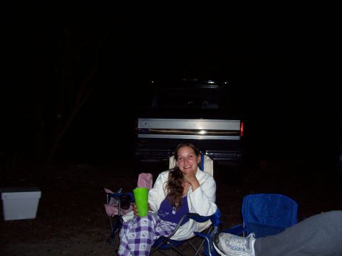 1994 Ford Bronco - A woman sits in a camping chair in front of the rear of a dark pickup truck at night.