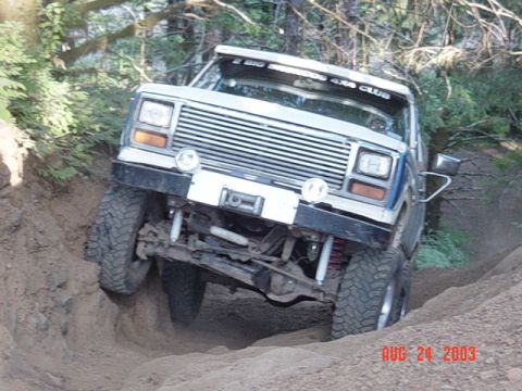 1989 Ford Bronco - Jeep Cherokee XJ navigating a steep dirt trail with one wheel in a rut.