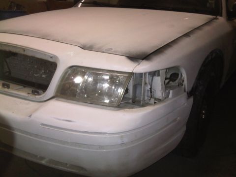 2003 Ford Crown Victoria - Front view of a white Ford Crown Victoria undergoing repairs, with visible damage to the headlight area and grille.