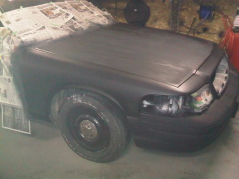 2003 Ford Crown Victoria - A 2003 Ford Crown Victoria is shown in a workshop, with its front end covered in newspaper and primer, ready for a new paint job.