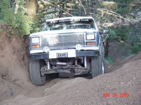 1989 Ford Bronco - A lifted Ford Bronco navigates a steep, sandy trail with trees in the background.
