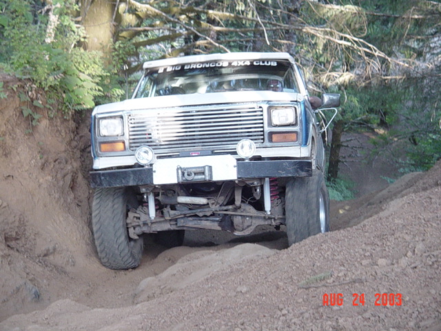 Lifted white and blue Ford Bronco climbing a dirt bank on a trail