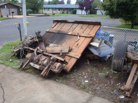 1989 Ford Bronco - A pickup bed removed and flipped upside down on the grass strip beside a suburban street, showing the wooden plank bed floor, cross sills,…