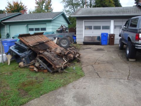1989 Ford Bronco - A scrap pile of rusty truck sheet metal, a wood-plank bed floor, a spare wheel and a blue tailgate heaped on the lawn beside a residential…