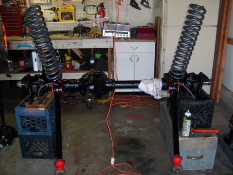 1986 Ford Bronco - Axle assemblies and coil springs are set up in a garage workshop.