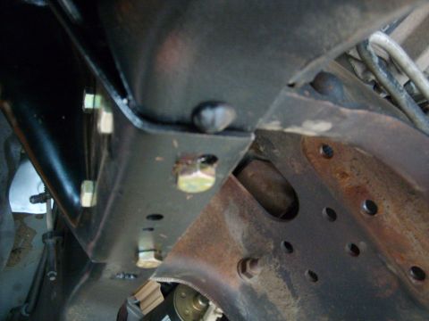 1986 Ford Bronco - Close-up view of underbody chassis components, showing bolted brackets and rusty metalwork. Supermotors.net logo is present.