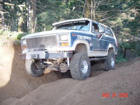 1989 Ford Bronco - A blue and white 1989 Ford Bronco tackles a challenging dirt path during an off-road excursion.