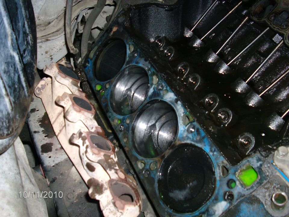 Engine block deck with head removed, exposed pistons in bores and removed cast-iron exhaust manifold