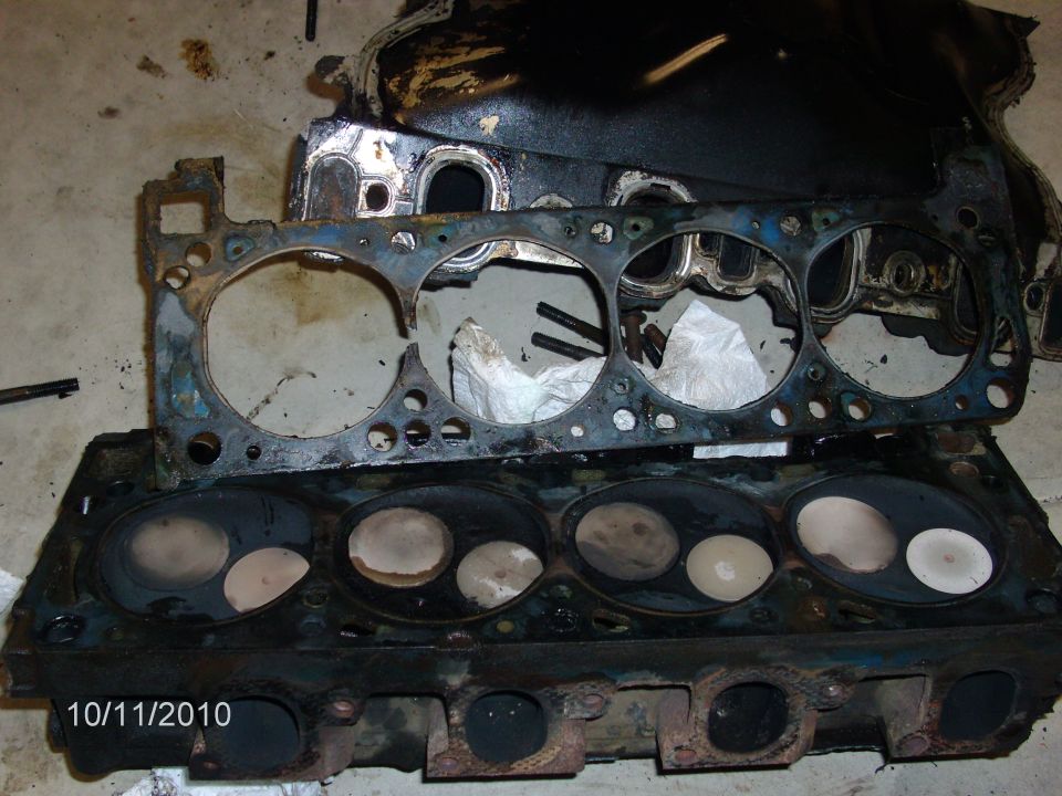 Cast-iron V8 cylinder head and used head gasket on garage floor during teardown