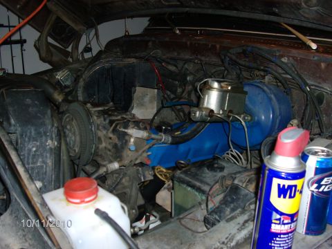 1979 Ford F-150 - The engine bay of a vehicle, blue valve covers and a prominent brake booster, with a can of WD-40 and a beer can visible.