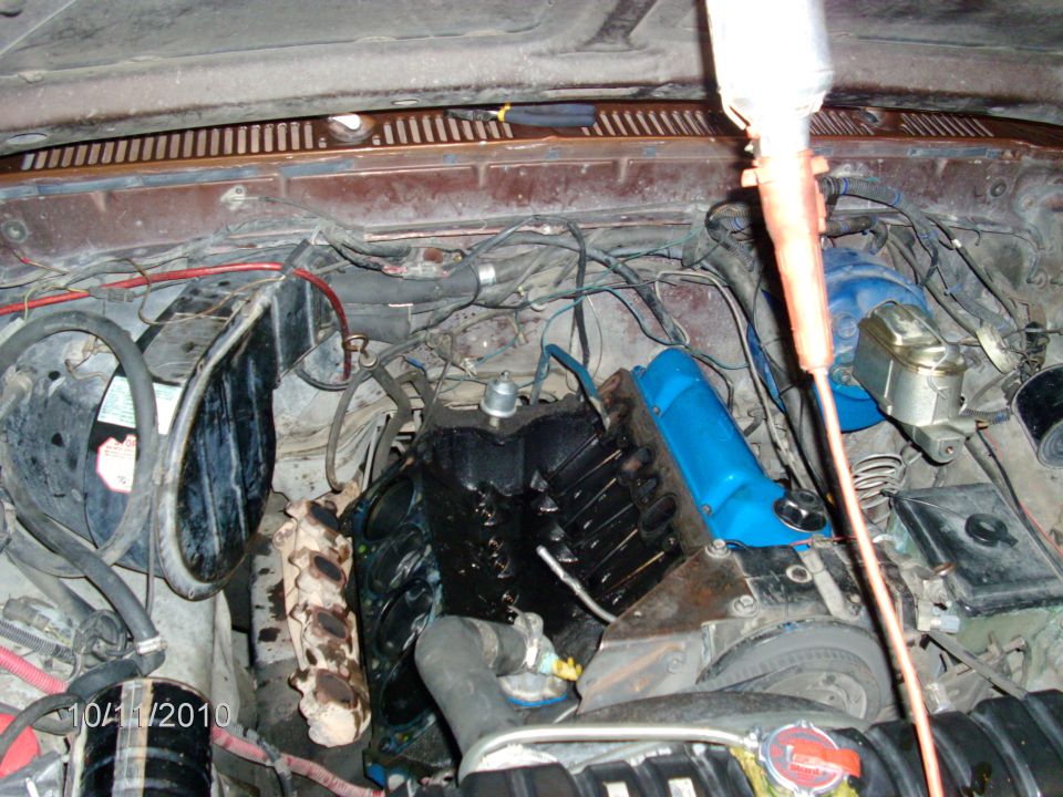 Engine bay with intake manifold removed, exposing V8 valley and pushrods; blue valve cover