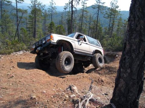 1990 Ford Bronco II - This modified Ford Bronco II navigates a challenging off-road terrain with its suspension and tires clearly visible.