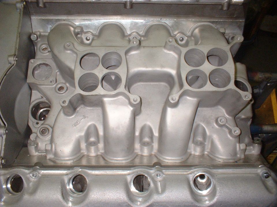 Close-up of an aluminum intake manifold with four carburetor mounting holes on each side