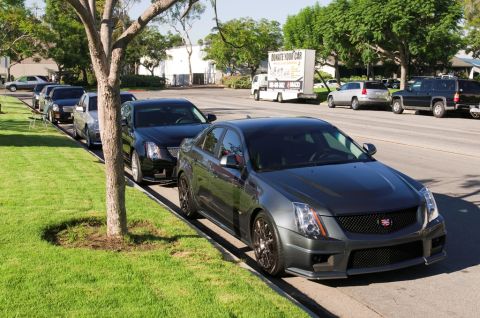 2006 Cadillac STS - Several Cadillacs are parked along a grassy curb on a sunny day. A truck with 'Donate Your Car' is visible in the background.