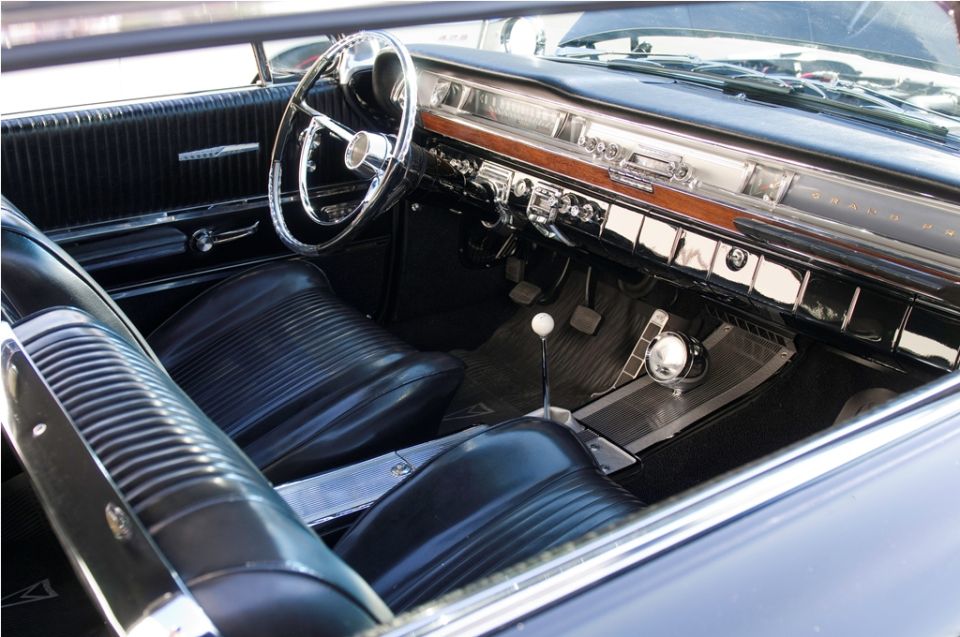 Interior view of a classic car with black vinyl seats, a large chrome steering wheel, and a wood-grain dashboard