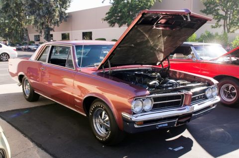 2006 Cadillac STS - A rose gold 1966 Pontiac GTO coupe is parked next to a red car, with its hood open to reveal the engine.