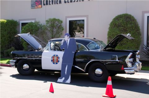 2006 Cadillac STS - This vintage police car, likely from the mid-1950s, is displayed with its hood and trunk open, alongside a cardboard cutout of a detective.