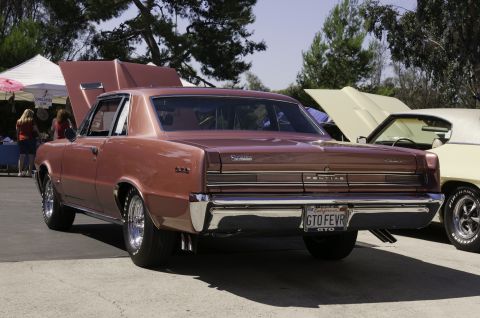2006 Cadillac STS - A classic 1964 Pontiac GTO coupe is parked next to another vehicle with its hood up.