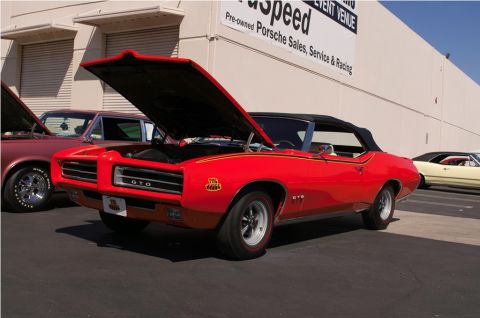 2006 Cadillac STS - A red 1969 Pontiac GTO convertible is displayed with its hood open, alongside other vehicles.