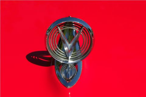 2006 Cadillac STS - A close-up of a vintage chrome hood ornament against a bright red background.