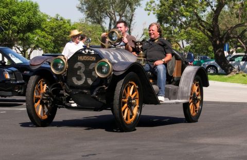 2006 Cadillac STS - Vintage Hudson race car with people riding in it, seen from the front.